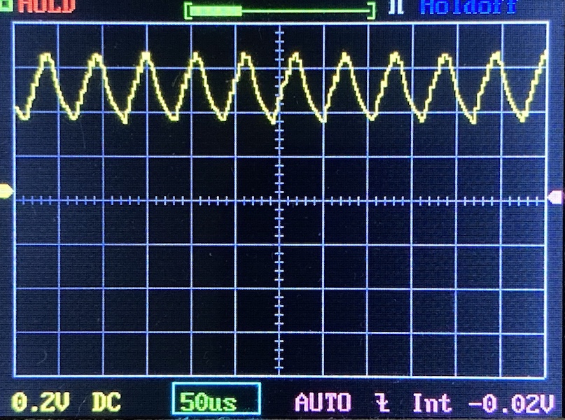 Oscilloscope screen displaying a yellow waveform with regular peaks and troughs on a grid. The settings show 0.2V DC, 50 microseconds per division, and automatic mode enabled.