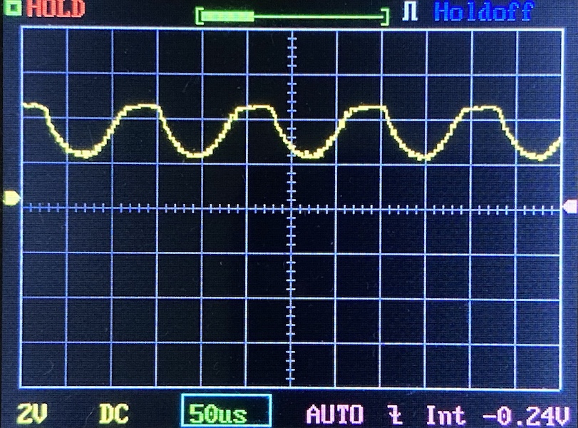 A digital oscilloscope screen displays a periodic yellow waveform with peaks and valleys. The horizontal axis shows 50 microseconds per division; the vertical axis shows 2 volts per division.