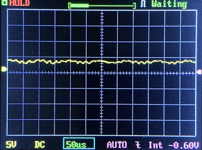 A digital oscilloscope screen displays a mostly flat yellow waveform near the center, with minimal noise. The settings show 5V per division, 50 microseconds per division, and a DC coupling. The screen reads HOLD and Waiting.