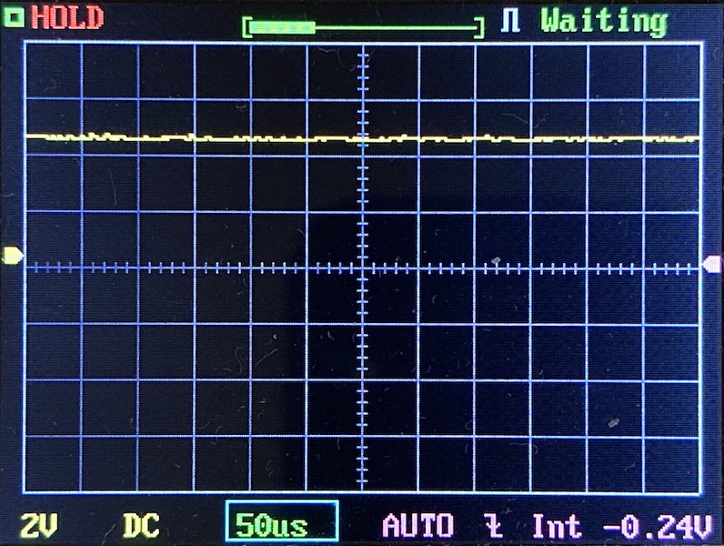 Digital oscilloscope screen showing a stable, nearly flat yellow waveform at the center, indicating minimal signal variation. The display reads HOLD and Waiting. Settings show 2V, 50μs, DC, AUTO, and -0.24V.