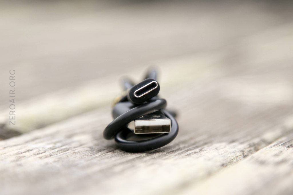 A coiled black charging cable with a USB-A connector and a USB-C connector resting on a wooden surface. The focus is on the ends of the cable.