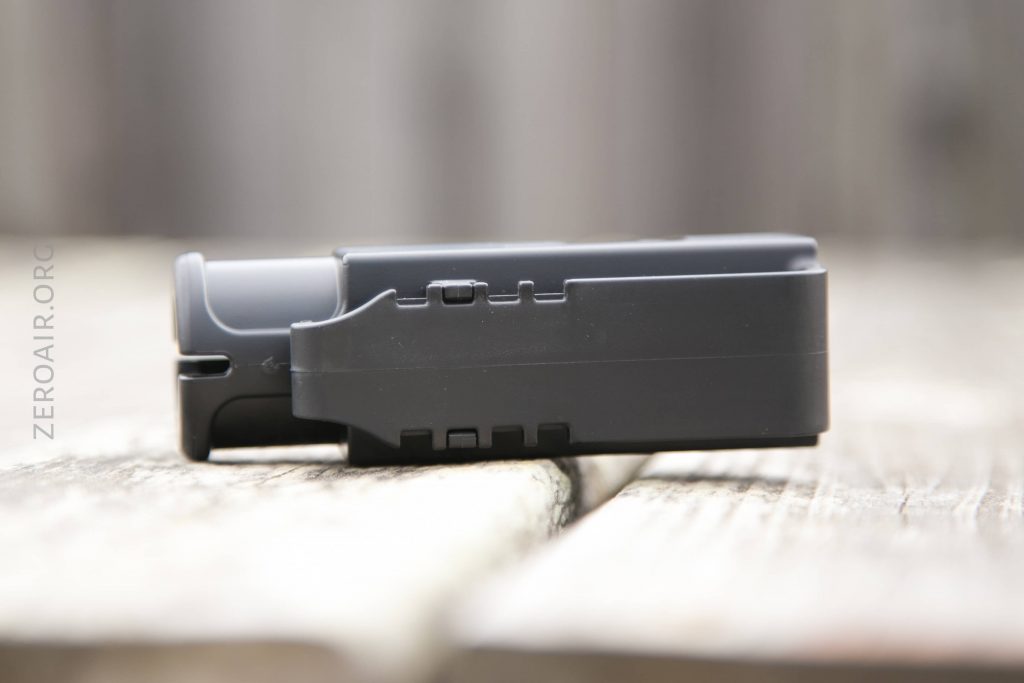A close-up side view of a black rectangular electronic device, possibly a battery or charger, placed on a wooden surface with a blurred background.