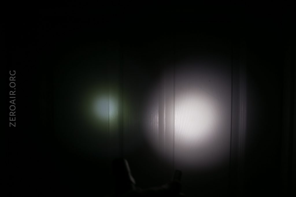 A white flashlight beam and a smaller green beam are projected onto a dark wall. The text ZEROAIR.ORG is faintly visible along the left side of the image.
