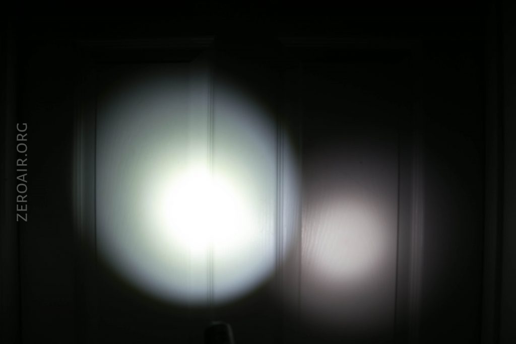 Two circular flashlight beams, one bright white and one dimmer, are projected onto a dark door. The website text ZEROAIR.ORG appears vertically on the left side of the image.