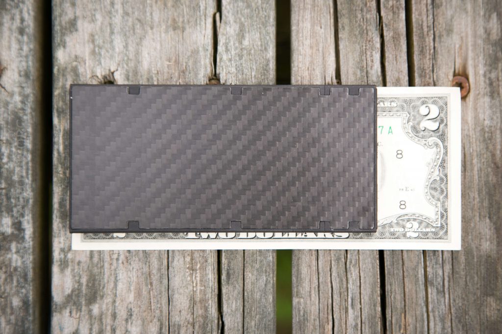A black rectangular card with a carbon fiber pattern lies on top of a two-dollar bill on a weathered wooden surface.
