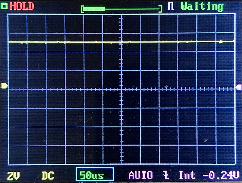 A digital oscilloscope screen displays a mostly flat yellow waveform near the zero line, grid lines, and status indicators including HOLD, Waiting, 2V, DC, 50 μs, AUTO, and -0.24V.