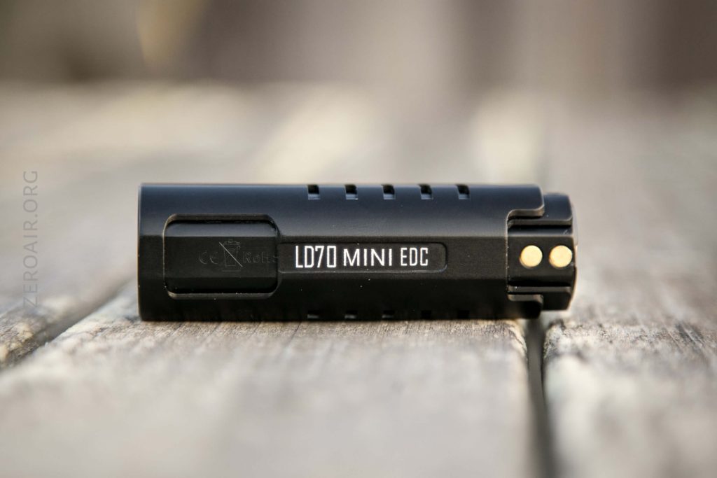 A small black cylindrical flashlight labeled LD70 MINI EDC lying on its side on a wooden surface, with gold contacts and vent holes visible.