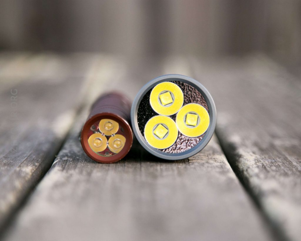 Close-up of two cylindrical objects lying on a wooden surface, showing their ends with three yellow circular components each, arranged in a triangular pattern.