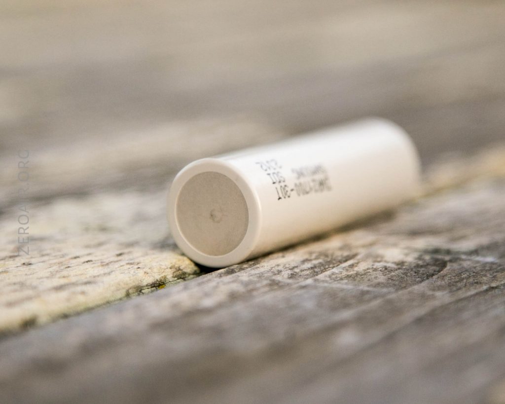 A close-up image of a white cylindrical object, possibly a battery or tube, lying horizontally on a wooden surface. The background is out of focus, drawing attention to the object in the foreground.
