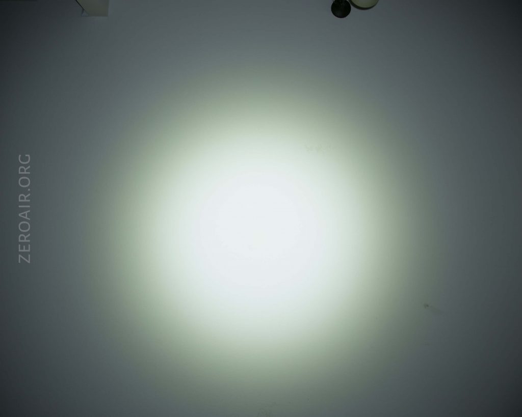 A bright white circular spotlight is centered on a plain wall with slight shadows and a faint gradient. The words ZEROAIR.ORG appear vertically on the left side.