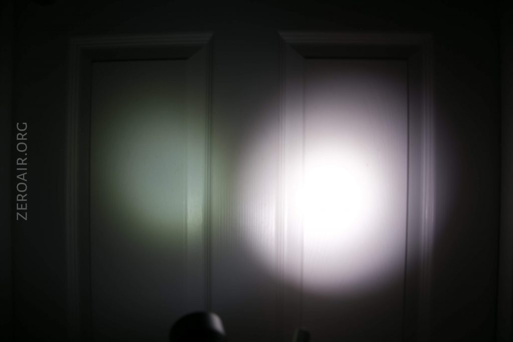 A white door is illuminated by two overlapping circles of light, one dimmer and greenish on the left and one brighter and whiter on the right. The text ZEROAIR.ORG appears vertically along the left side.