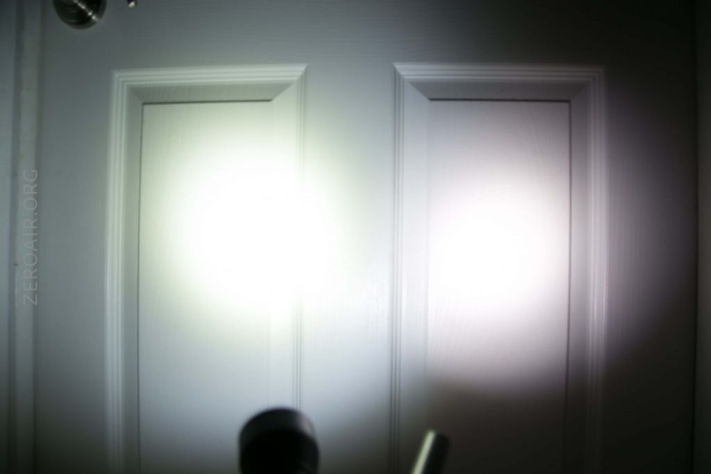 A white door with rectangular panels is illuminated by two bright flashlight beams, one on each panel. The flashlights are partially visible at the bottom of the image.