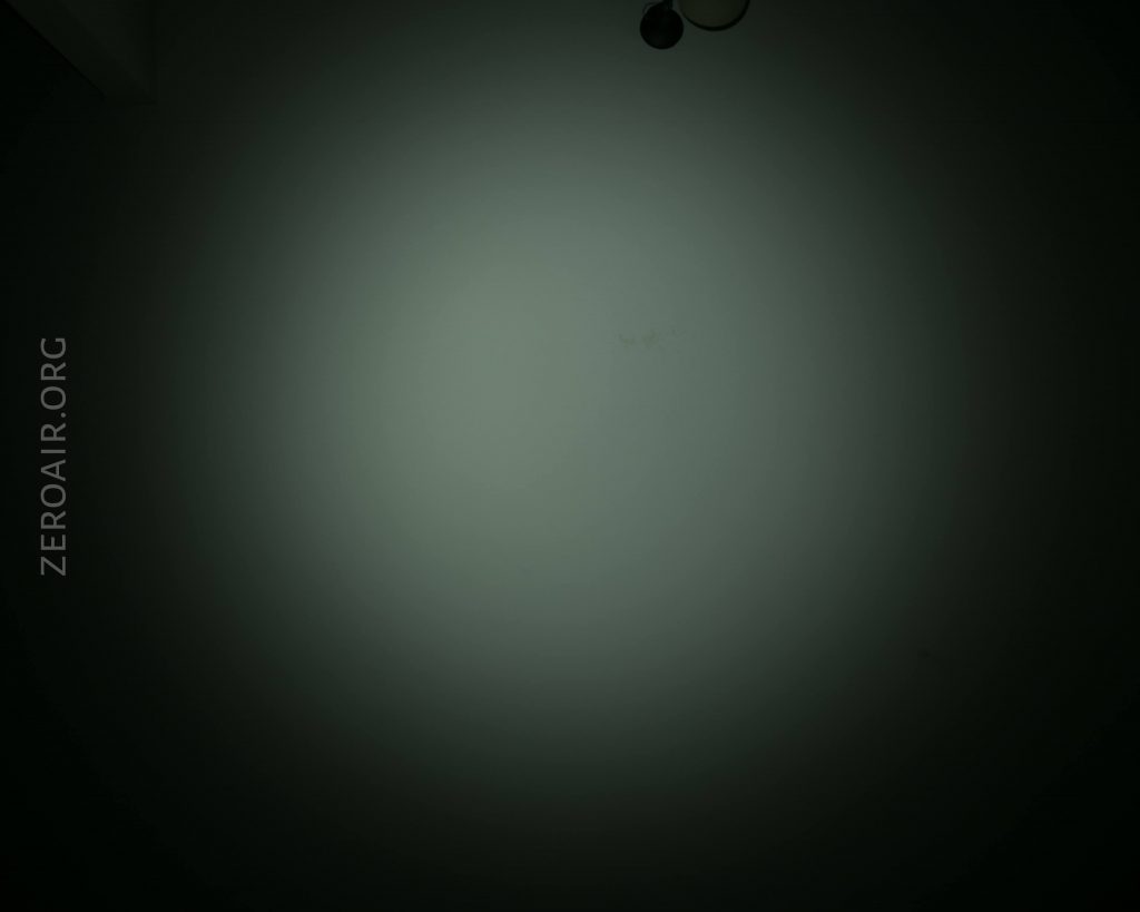 A dim, circular beam of light is shown against a dark background. The image features the text ZEROAIR.ORG vertically along the left side. There are two small, round objects near the top right corner.