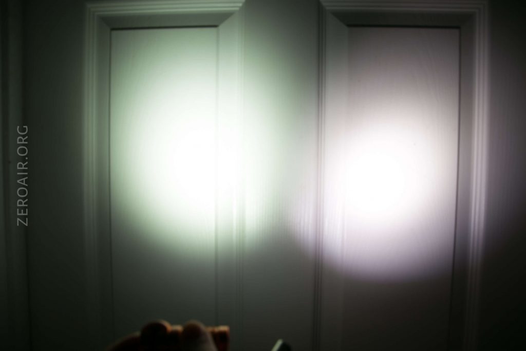 Two beams of light from flashlights are shining on a white paneled door, creating overlapping circular patterns of illumination. A hand is partially visible holding one flashlight at the bottom left of the image.