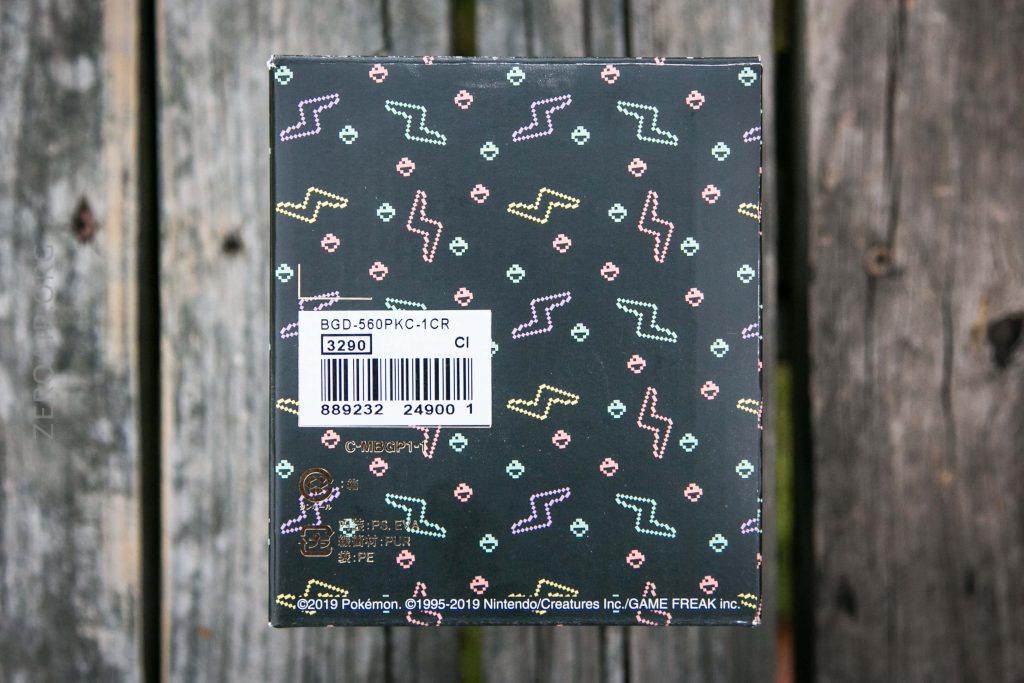 A close-up of a black box with colorful zigzag and dot patterns, a barcode sticker with product information, and Pokémon branding on a weathered wooden surface.
