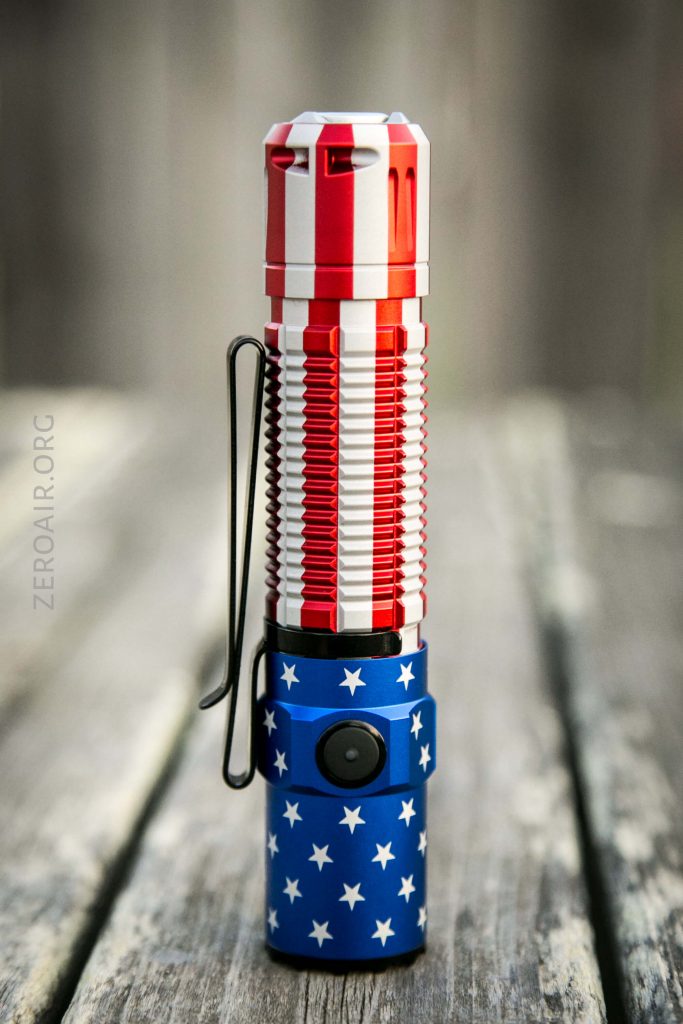 A flashlight with a design resembling the American flag, featuring red and white stripes on the top half and white stars on a blue background on the bottom half, standing upright on a wooden surface.