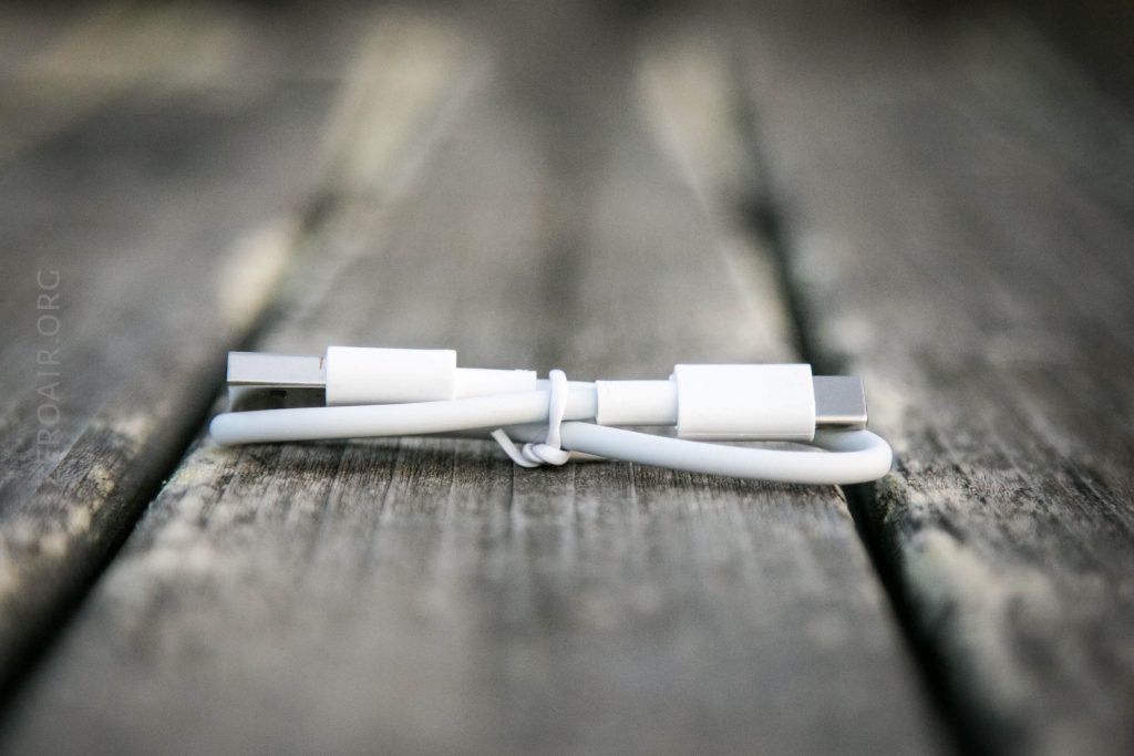 A white USB-C charging cable is coiled and secured with a small wire, resting on a weathered wooden surface with a blurred background.