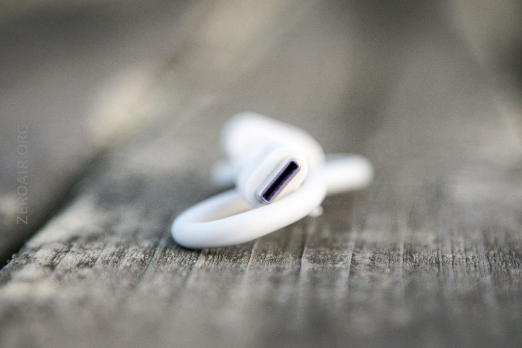A close-up of a white USB-C charging cable resting on a wooden surface, with the connector end in focus and the background blurred.