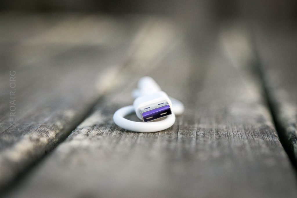 A white USB cable with a purple connector lies coiled on a weathered wooden surface, with the focus on the connector and the background blurred.