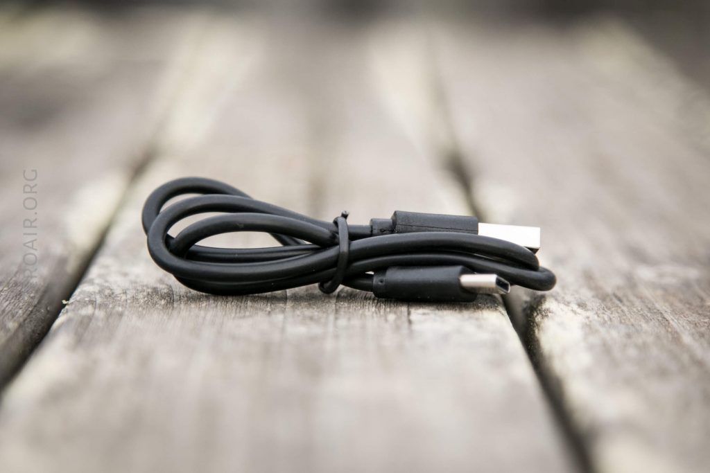 A black USB cable is coiled neatly and placed on a wooden surface with a blurred background.
