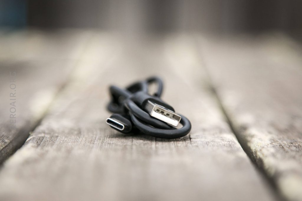 A black USB cable with both USB-A and USB-C connectors lies coiled on a weathered wooden surface, photographed with a shallow depth of field.