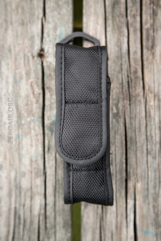 A black nylon case with a flap closure is placed vertically on a weathered wooden surface. The stitching and texture of the fabric are visible.