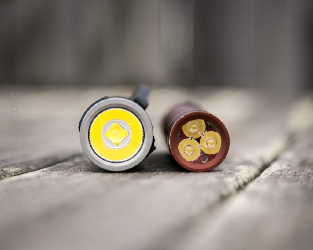 Two flashlights are lying on a wooden surface, shown from the front. The flashlight on the left has one LED, while the flashlight on the right has four smaller LEDs arranged in a circle.
