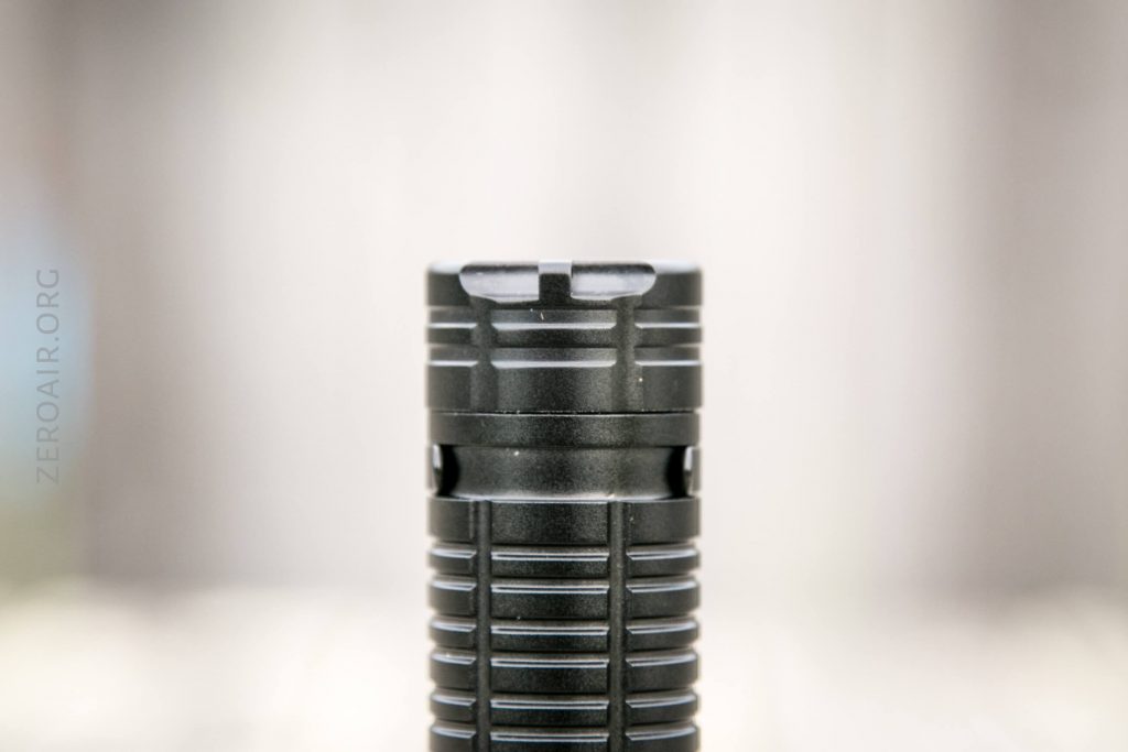 A close-up image of the upper section of a black, ribbed cylindrical object, likely a flashlight, set against a blurred, neutral background. The object is centered in the frame with ZEROAIR.ORG faintly visible on the left.