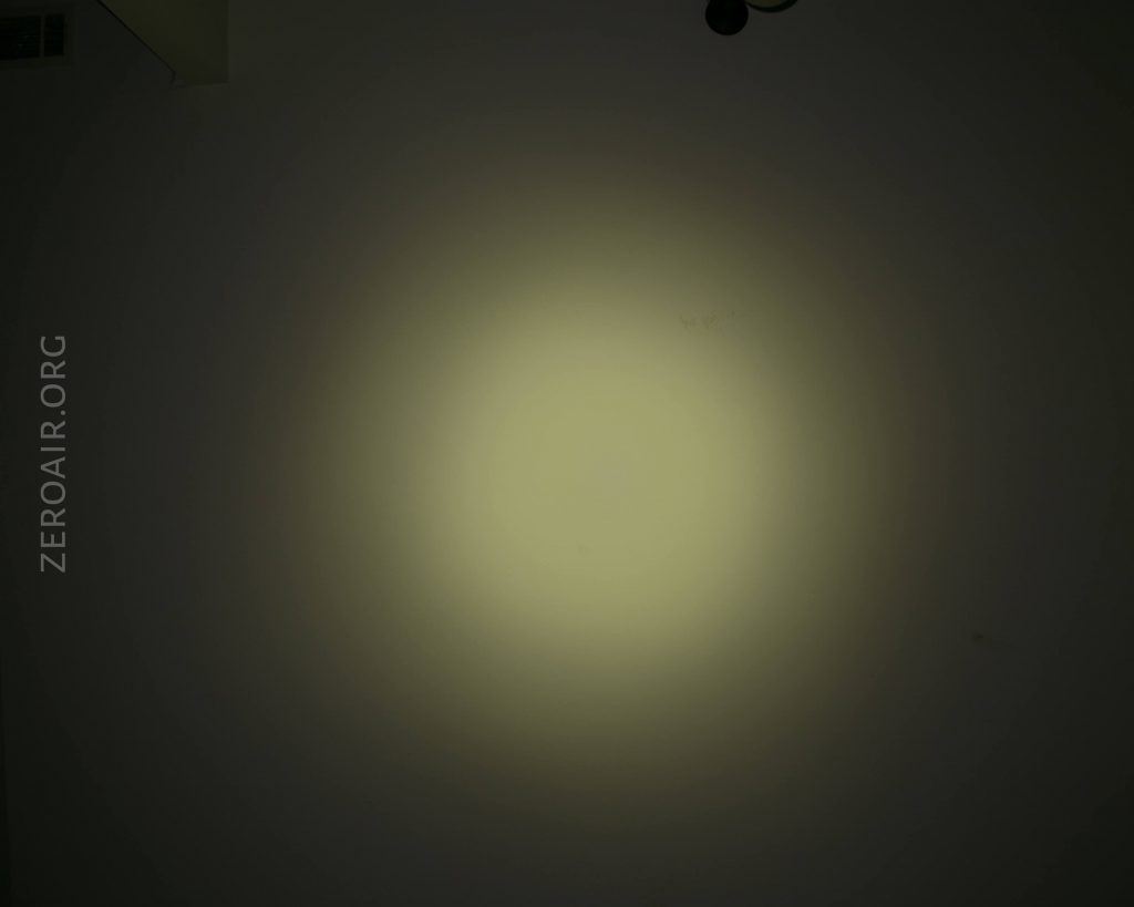 A circular beam of light is projected onto a dark wall, creating a bright center with a fading halo. The text ZEROAIR.ORG appears vertically along the left side of the image.