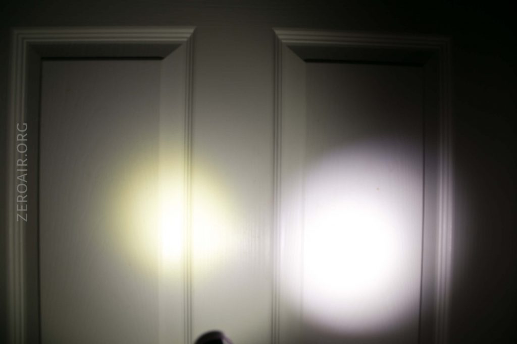 A closed white door is illuminated by two flashlight beams, one yellowish on the left and one white on the right. The background and surroundings are dim. The text ZEROAIR.ORG is visible on the left side.