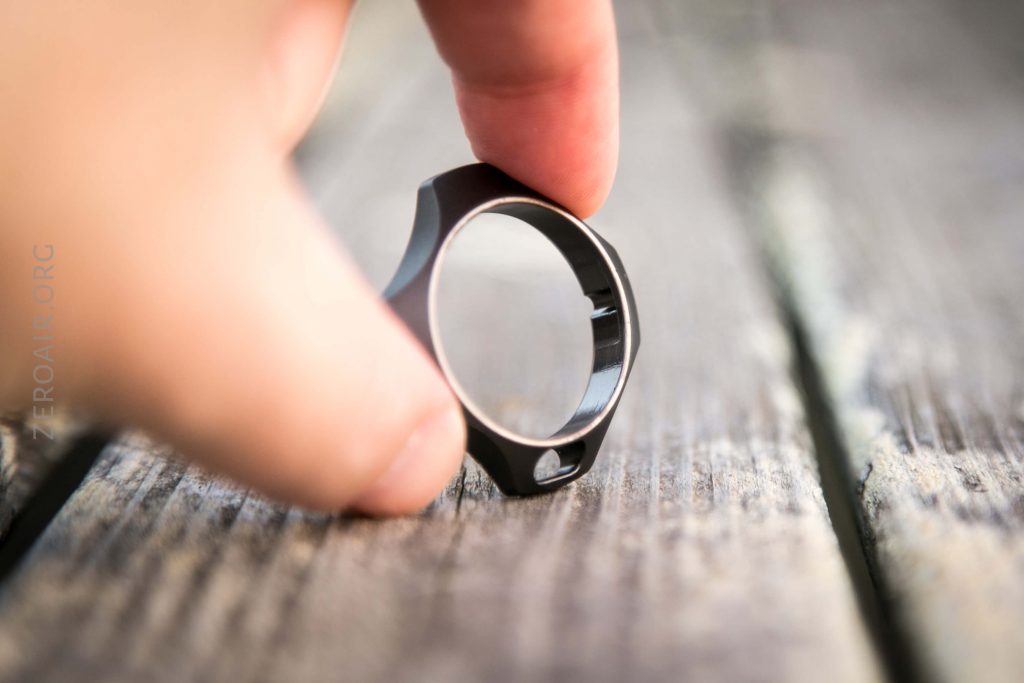 A hand holds a metallic, circular object resembling a ring with a keyhole-shaped cutout at its base, placed on a weathered wooden surface.
