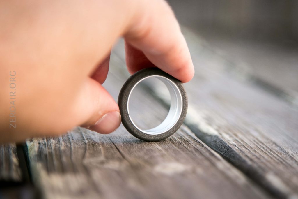 A hand holding a small round object with a metallic outer ring and white inner ring, resting on a weathered wooden surface.
