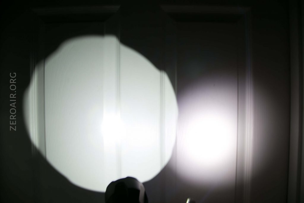 A flashlight beam creates a large, round area of bright light on a closed door. A smaller, dimmer beam is visible to the right. The text ZEROAIR.ORG is seen vertically on the left side.
