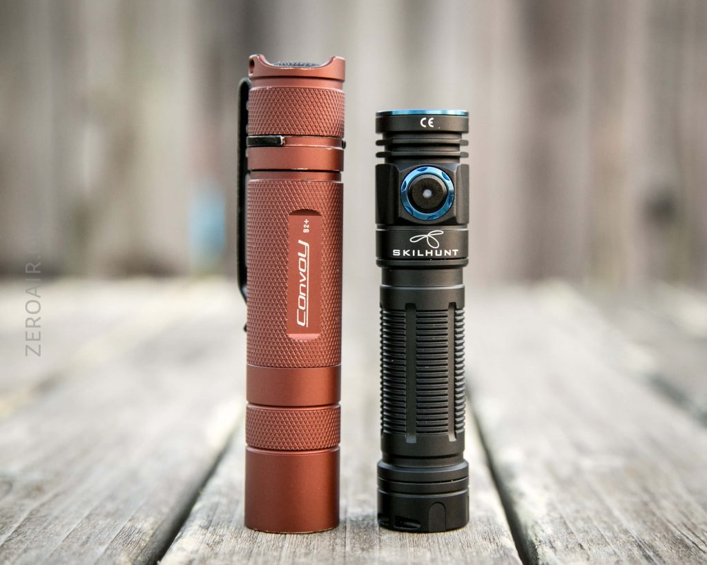Two flashlights stand upright on a wooden surface. The one on the left is red with Convoy branding, and the one on the right is black with Skilhunt branding and a blue circular button. The background is blurred.