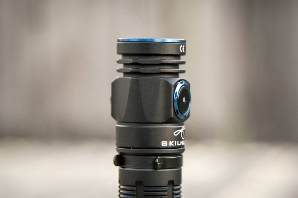 A close-up of a black SKILHUNT flashlight standing upright, showing its ridged head, side button, and some branding on the body, set against a blurred neutral background.