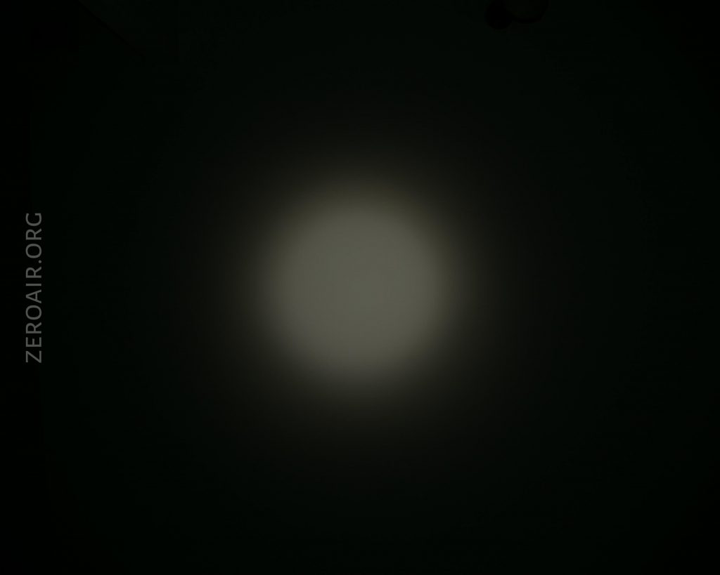 A dim, circular beam of light is projected onto a dark surface. The text ZEROAIR.ORG appears vertically along the left edge of the image.