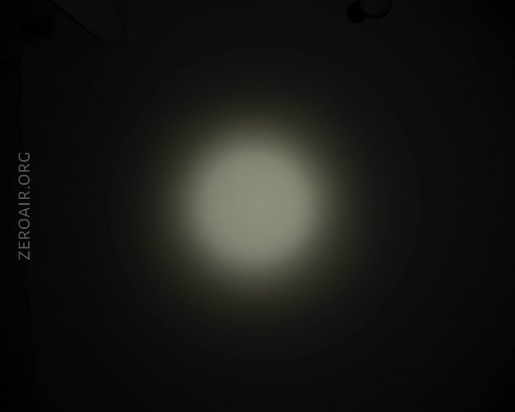A circular white light is projected onto a dark surface with the text ZEROAIR.ORG vertically along the left side of the image.