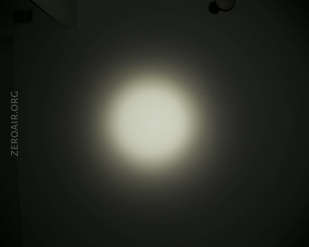A circular beam of white light is projected onto a dark surface, gradually fading at the edges. The text ZEROAIR.ORG is vertically positioned on the left side of the image.