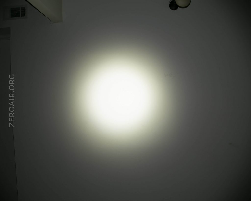 A bright circular beam of white light is projected onto a plain wall in a dark room. The words ZEROAIR.ORG appear vertically along the left side of the image.