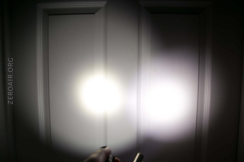 Two white beams of light from flashlights are projected onto a white paneled door in a dark room. A hand holding one flashlight is visible at the bottom of the image. The text ZEROAIR.ORG appears on the left side.