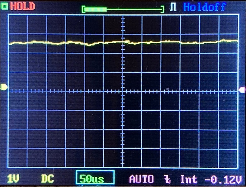 Oscilloscope screen showing a mostly flat yellow waveform near the center, with grid lines, horizontal and vertical axis markers, and labels reading 1V, DC, 50μs, AUTO, and -0.12V.