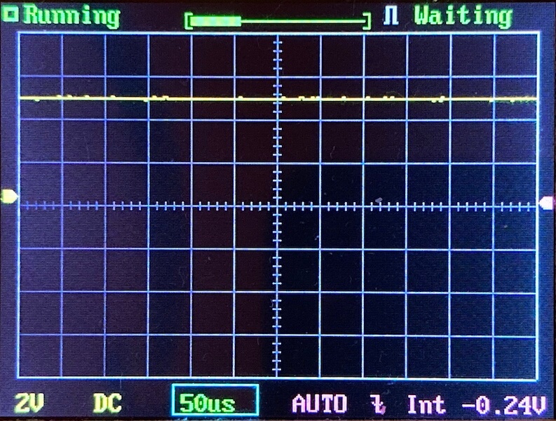 A digital oscilloscope screen displays a mostly flat yellow waveform near the top, gridlines, and indicators showing Running, 2V DC, 50 microseconds, AUTO mode, and a baseline voltage of -0.24V.