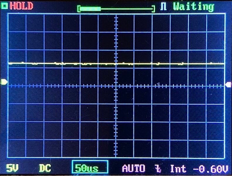 Oscilloscope screen displaying a flat yellow trace near the center, HOLD and Waiting indicators active, with settings shown as 5V/div, DC coupling, 50 microseconds per division, and -0.60V baseline.
