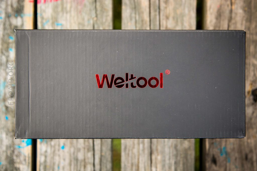 A black rectangular box with the word Weltool in red lettering on the top, placed on a wooden surface with visible grain and some blue paint marks.