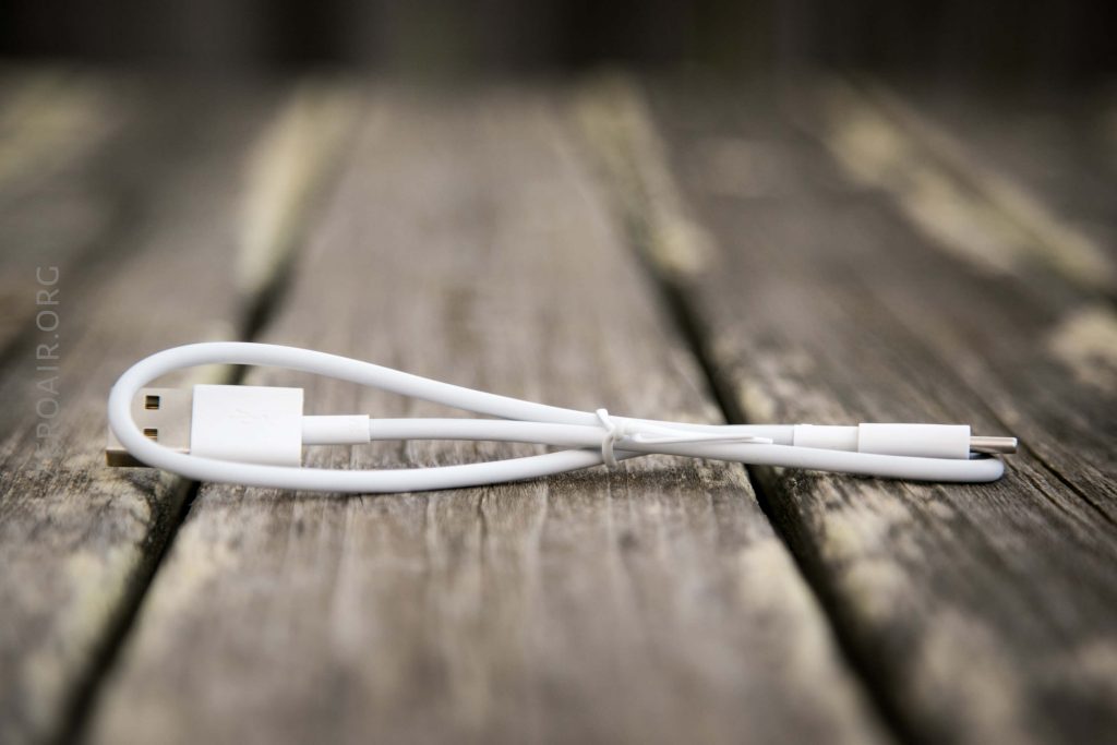 A white USB cable with one end having a USB-A connector and the other a USB-C connector, lying on a wooden surface with a blurred background.
