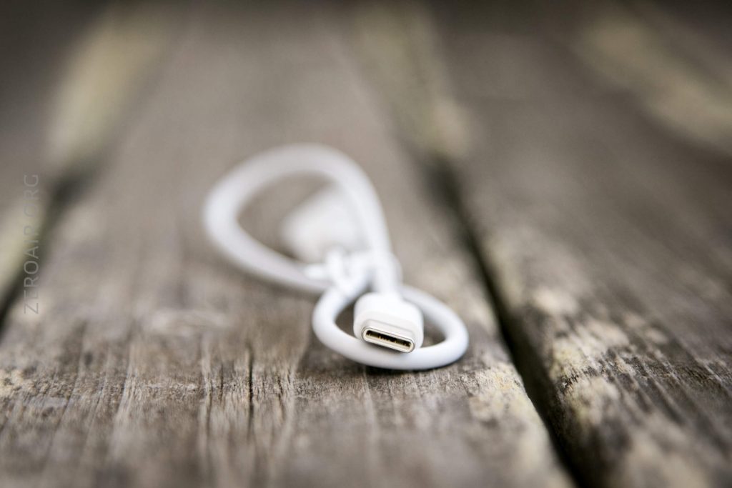 A white USB cable is laid on weathered wooden planks, with the USB connector in focus in the foreground and the blurred cable extending back.
