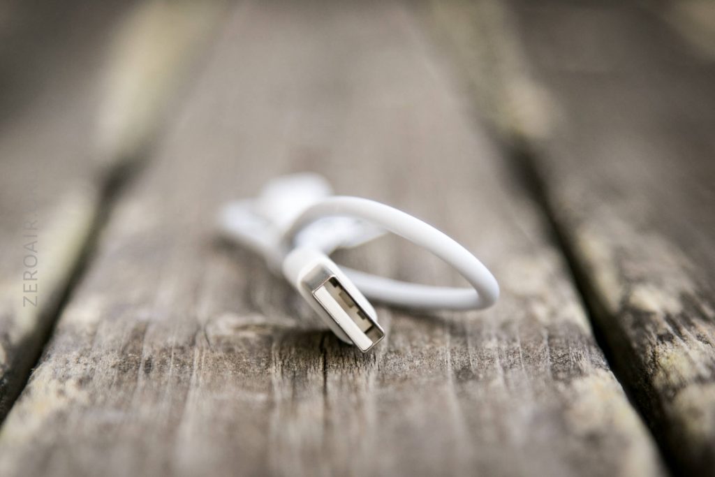 A white USB cable lying on a weathered wooden surface, with the USB connector facing the camera and the background out of focus.