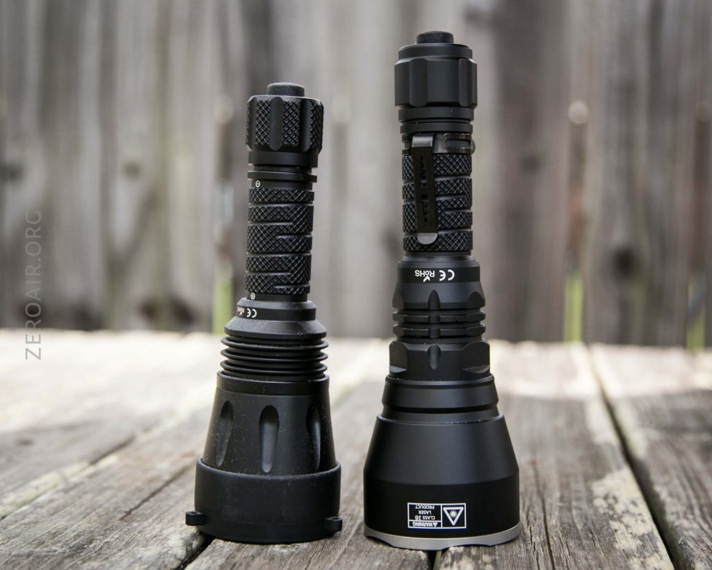 Two black, heavy-duty LED flashlights stand upright on a weathered wooden surface, positioned side by side in front of a blurred wooden fence background.