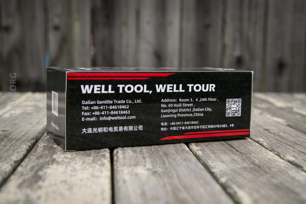 A black rectangular product box with the text WELL TOOL, WELL TOUR and company contact information printed in white and red, placed on a wooden surface with a blurred wooden fence in the background.