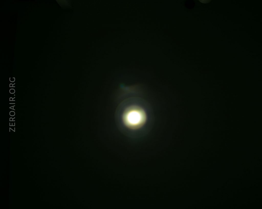 A bright white circle of light appears in the center of a dark background with faint halos around it. The text ZEROAIR.ORG is written vertically along the left side of the image.